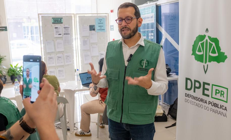 Imagem em que se vê o Defensor Público falando sobre os serviços oferecidos pela DPE-PR no Registre-se. Ao se ado é possível ver o banner com a logo da instituição.