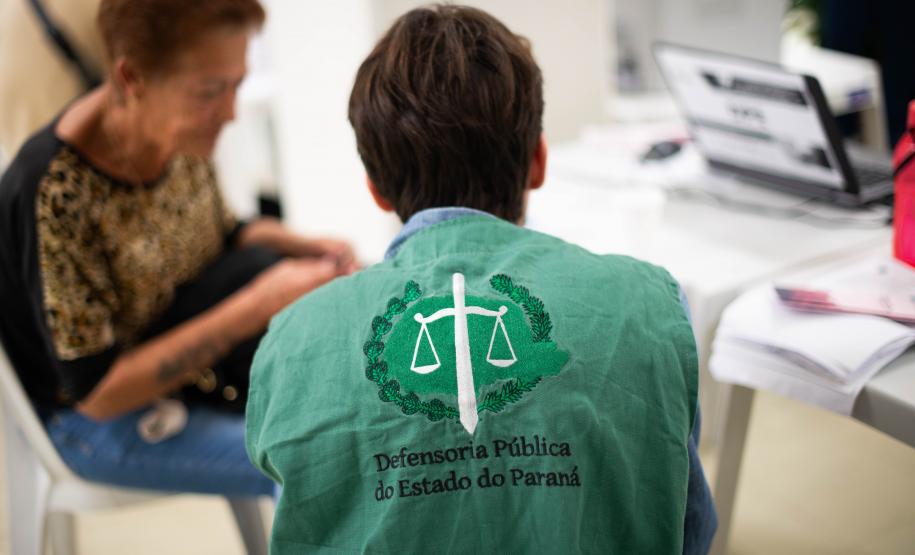 Servidor da Defensoria Pública usando coleta com a logo da instituição realiza atendimento de senhora idosa durante mutirão de atendimento.
