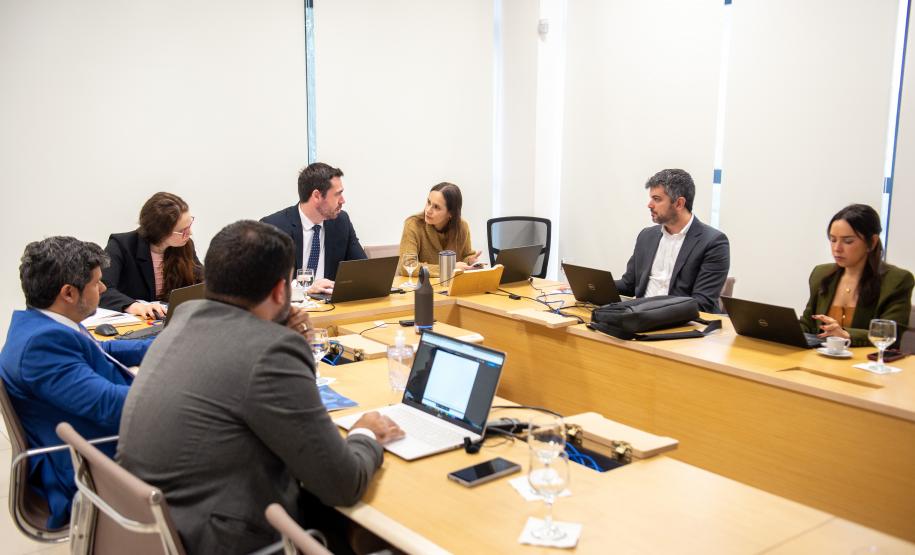 Imagem mostra um grupo de sete pessoas sentadas a mesa com laptops.