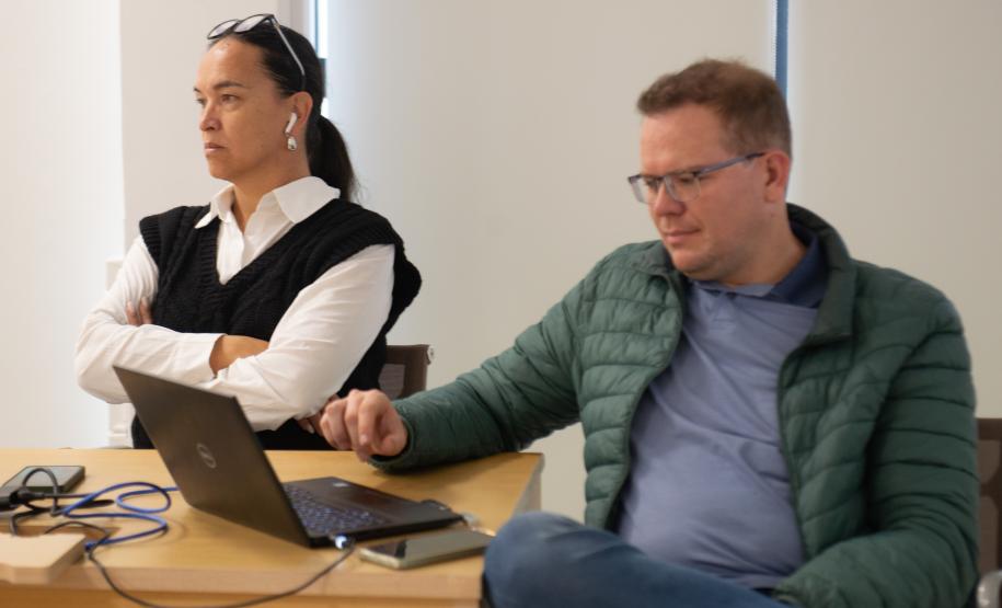 Imagem de duas pessoas, um homem e uma mulher trans sentados a mesa.