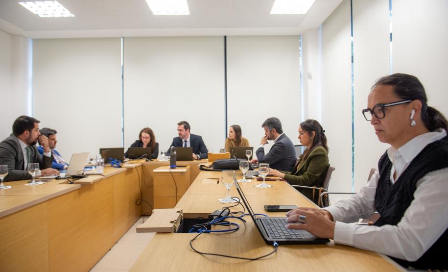 Em primeiro plano se vê uma mulher trans ao computador e ao fundo estão outras oito pessoas, todas ao computador.