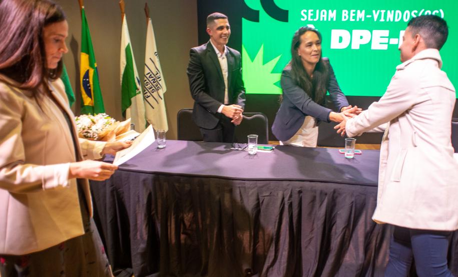 Servidor cumprimenta a autoridades na mesa da cerimônia de posse.