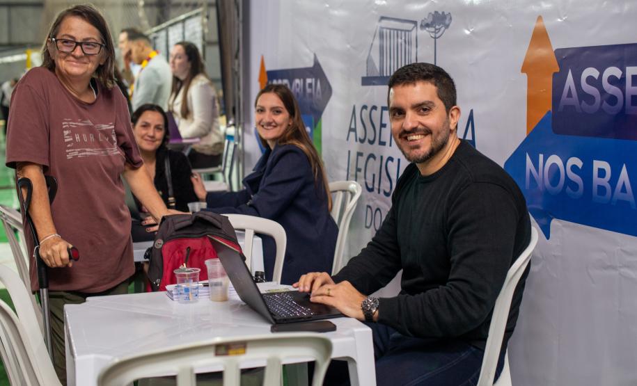 Equipe da DPE-PR posa para foto com assistidos. Quatro pessoas aparecem na foto, três sentadas e uma de pé se apoiando em muleta.
