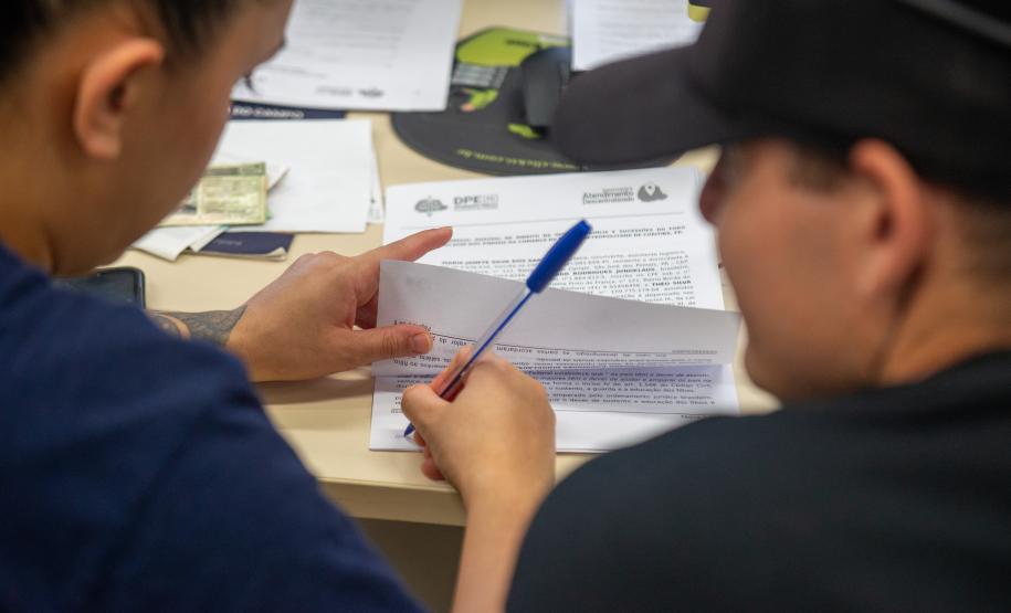 Imagem mostra detalhe de casal assinando documentos durante Mutirão da Defensoria.