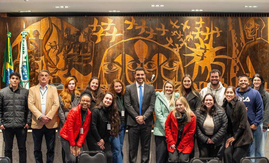 Equipe que atuou no Mutirão da DPE-PR na ALEP posa para foto em frente ao painel de madeira do Plenarinho.