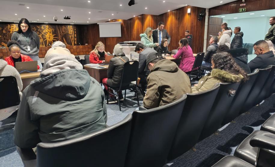 Um grupo grande pessoas, algumas sentadas outras em pé, aguardam o atendimento da Defensoria Pública do Paraná durante o Mutirão na ALEP. Ao fundo os atendimentos.