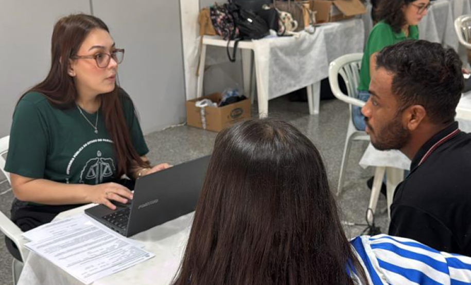 Imagem mostra servidora da DPE-PR realizando atendimento de um casal. A mulher está de costas em primeiro plano e ao fundo homem fala com a servidora.