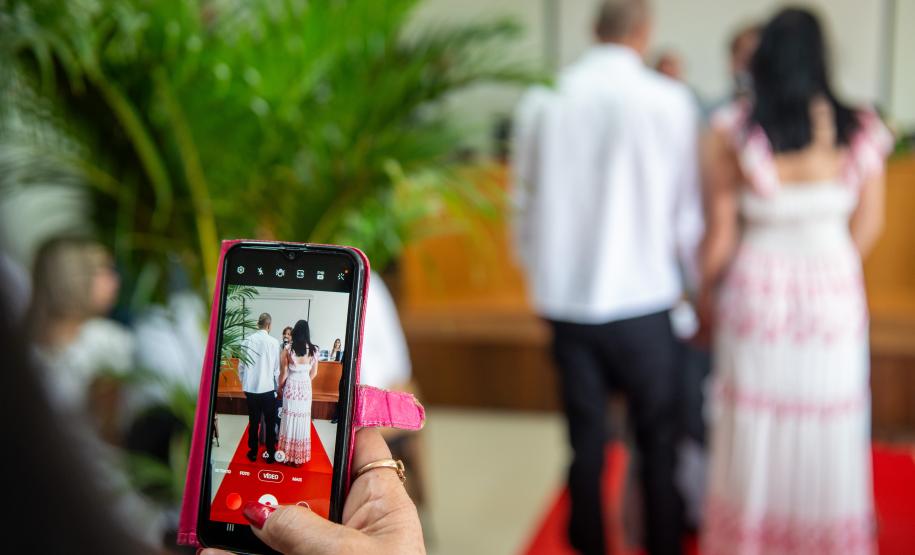 Em primeiro plano celular grava casal que está diante do juiz de paz.