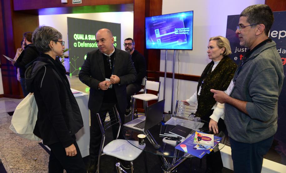 Quatro pessoas, dois homens e duas mulheres, conversam em frente a um stand da feira do Enastic.