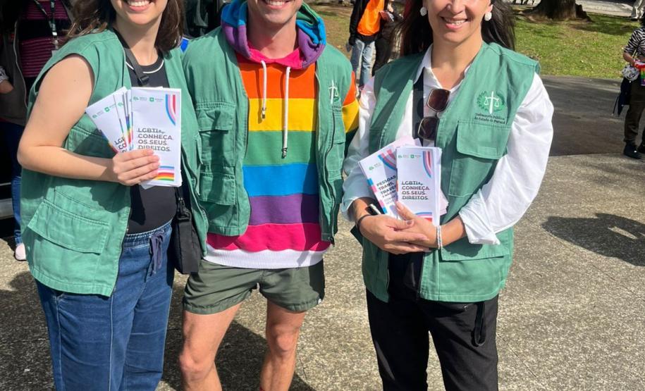 Servidoras e defensor público, utilizando coletes da Defensoria Pública, mostrando materiais informativos sobre a retificação de prenome e gênero.