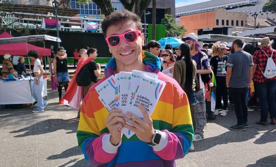 Defensor público, utilizando colete da Defensoria Pública, mostrando materiais informativos sobre a retificação de prenome e gênero.