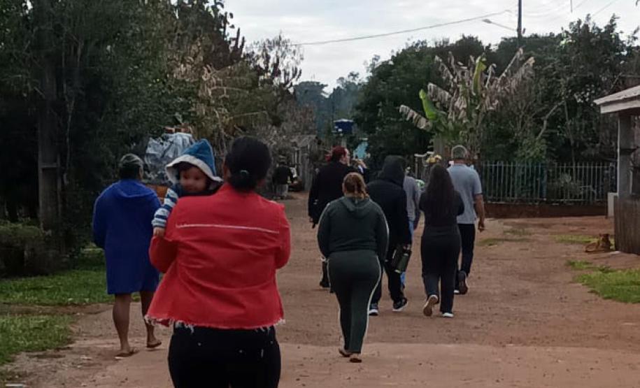 Imagem mostra um grupo de pessoas caminhando por rua de barro. No primeiro plano uma mulher carrega um bebê.