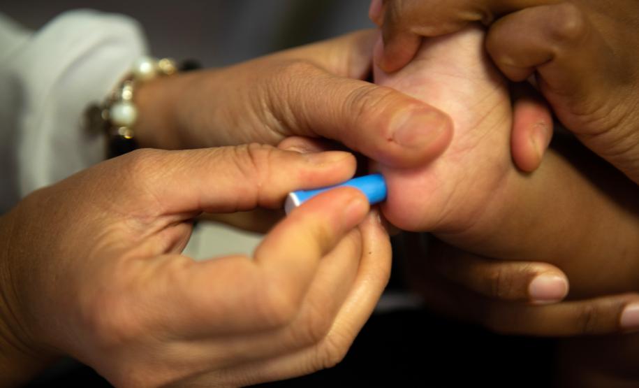 Imagem em close mostra enfermeira colhendo amostra do pé de uma criança pequena para exame de DNA no Mutirão Meu Pai Tem Nome da DPE-PR.
