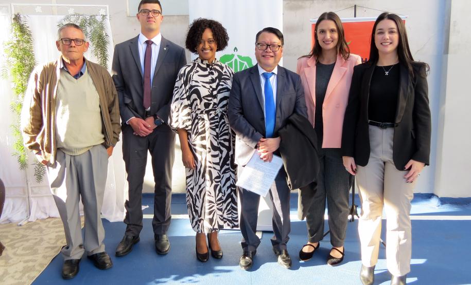 Imagem que mostra defensores públicos com o juiz Osvaldo Taque. É um grupo com seis pessoas, composto por homens e mulheres vestidos formalmente. Eles estão em pé em um pátio azul, com a decoração do casamento ao fundo.