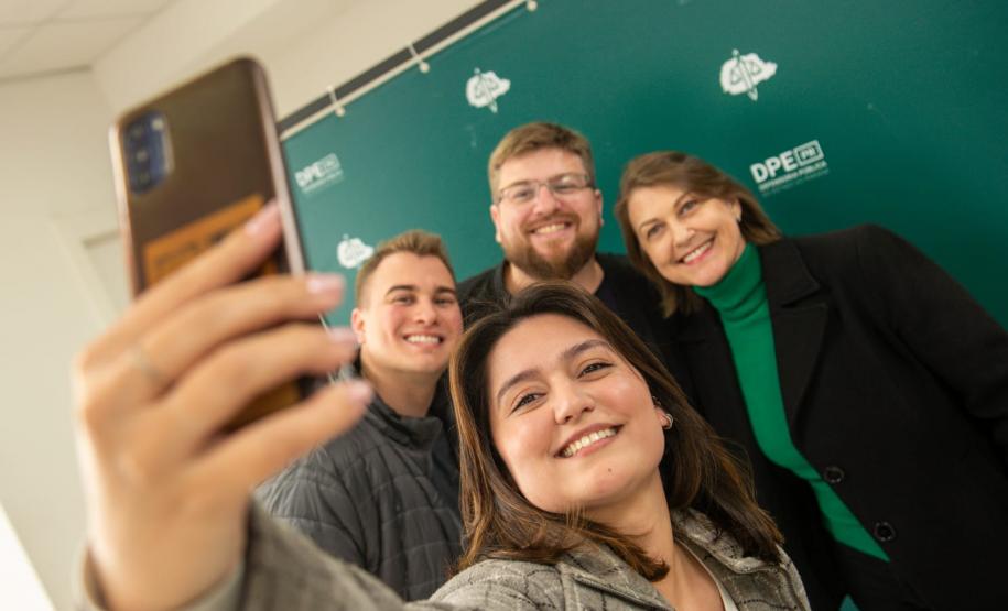 Servidor empossado hoje posa para selfie com a família em frente a backdrop da Defensoria.