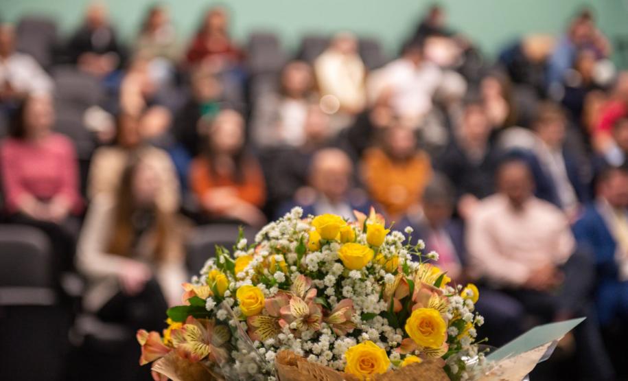 Em primeiro plano flores e ao fundo auditório lotado com familiares dos novos servidores.