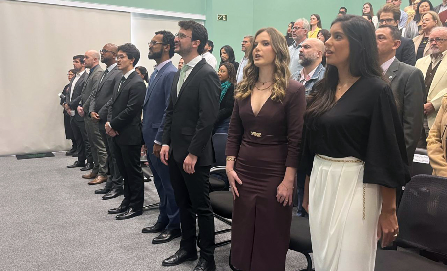 Novos defensores públicos e o público presente no auditório da Defensoria acompanham o hino nacional durante a solenidade de posse.
