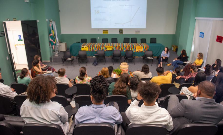 Imagem mostra o auditório da DPE-PR com várias pessoas acompanhando o observatório de violência contra a mulher indígena.