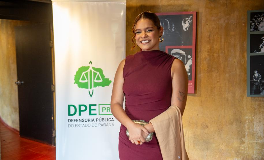 Defensora empossada na cerimônia posa ao lado do banner antes da cerimônia.