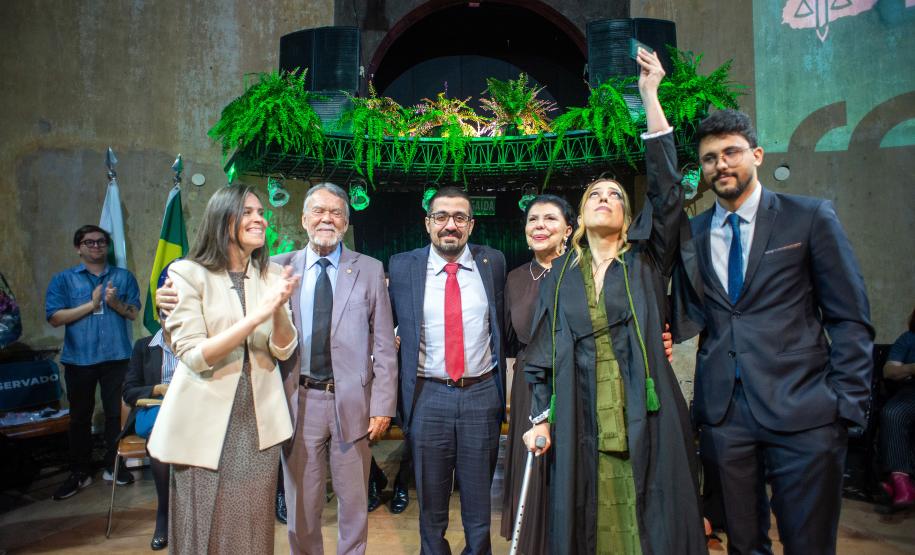 Defensora Pública empossada posa ao lado da família. Ela ergue a carteira funcional numa homenagem ao pai falecido.