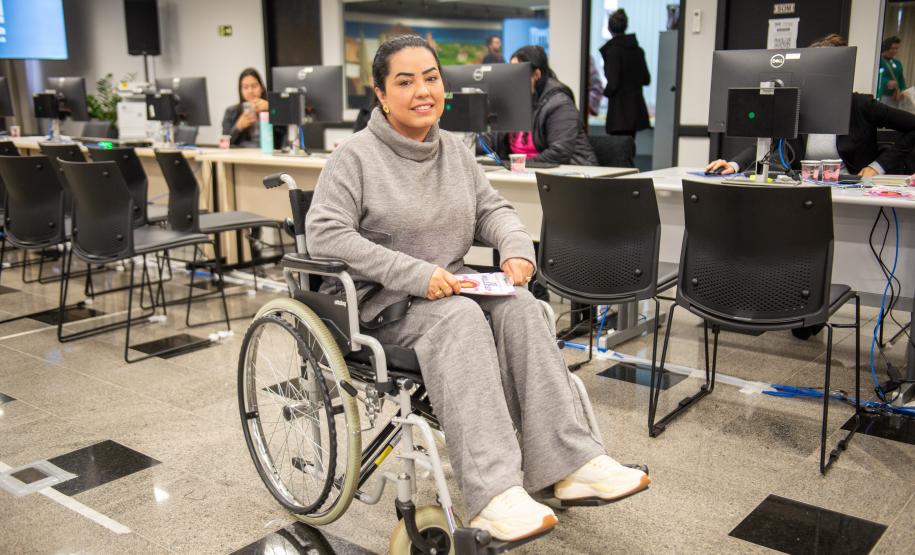 Uma mulher sentada em cadeira de rodas posa para foto durante o Mutirão de Saúde da Defensoria na Camara Municipal de Curitiba.