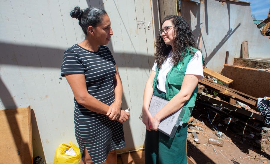 Psicóloga da Defensoria Pública realiza escuta qualificada de uma mulher vítima do tornado em Rio Bonito do Iguaçu. O cenário da conversa é a casa destruída pelo vento.