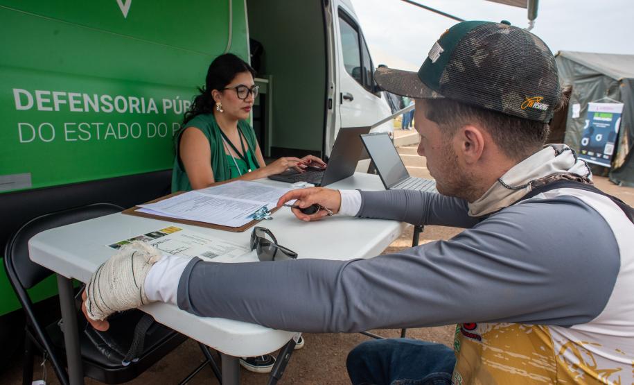 Assistente jurídica da Defensoria Pública realiza atendimento  na Van de Direitos de um homem com curativo na mão esquerda.