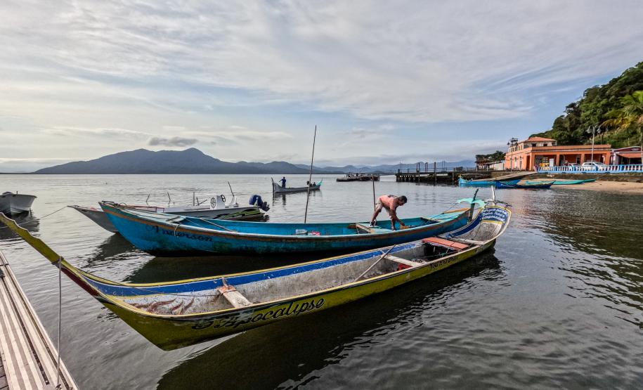 Imagem mostra canoas atracadas no pier, ao fundo um pescador prepara o barco para partir.