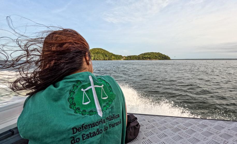 Defensor Público de costas usando colete da instituição está em um barco indo em direção à Guaraqueçaba.
