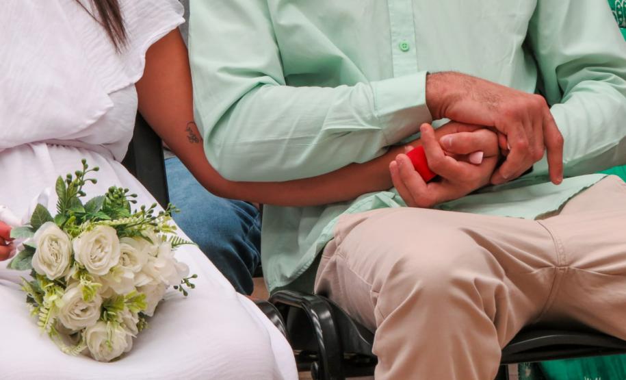Detalhe das mãos dos noivos entrelaçadas. A noiva segura um buquê de flores.