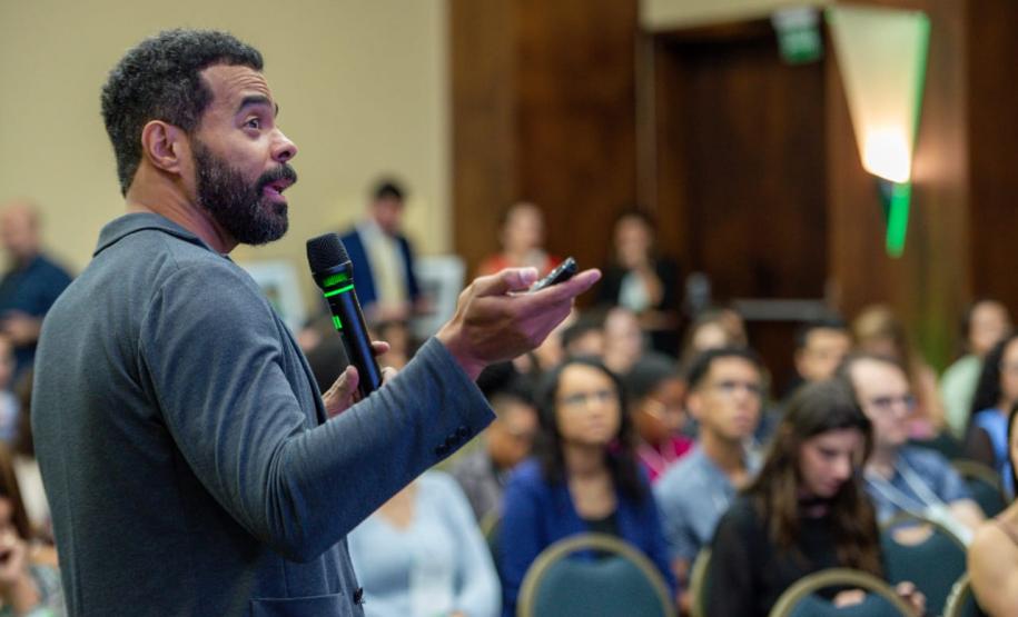 Homem negro em primeiro plano fala para uma plateia ao fundo desfocada. Palestra com especialista do Google sobre uso da Inteligência Artificial.