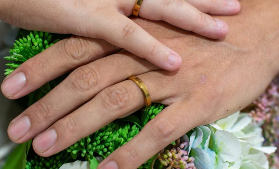 Detalhe das mãos com alianças sobre um buquê de flores.