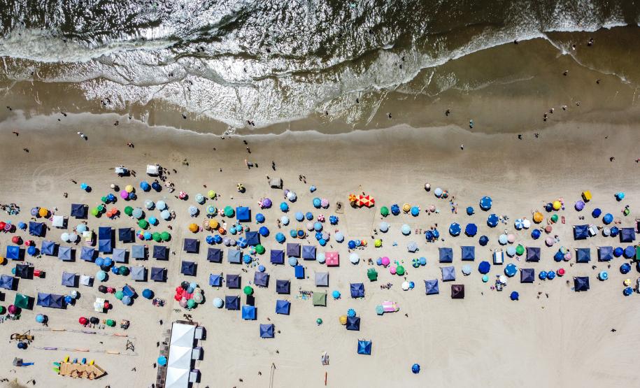 Imagem aérea mostra a orla de Caiobá com vários guarda-sóis vistos de cima na beira da praia.