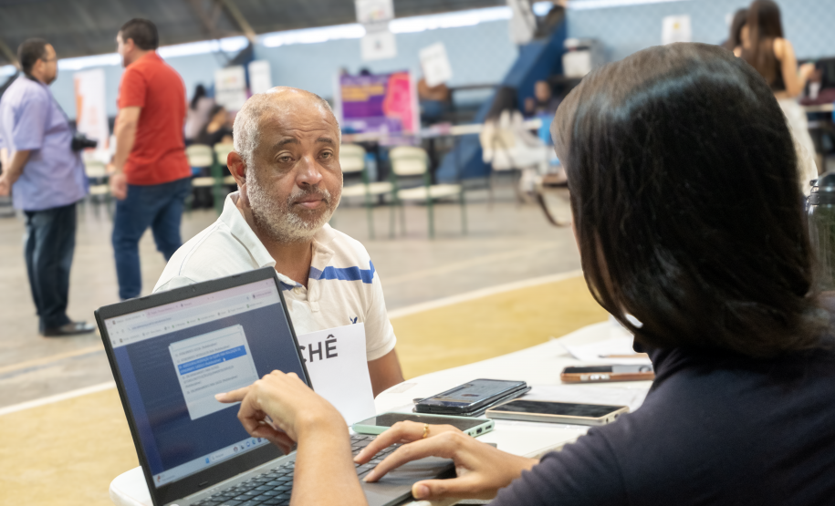 Imagem mostra um homem negro sentado na mesa com servidor que realiza o atendimento durante um Mutirão da Defensoria Pública do Paraná.