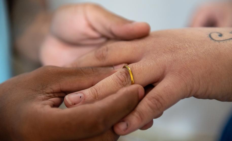 Imagem mostra detalhe de noivo colocando aliança na mão da noiva durante cerimônia do Casando Direitos.