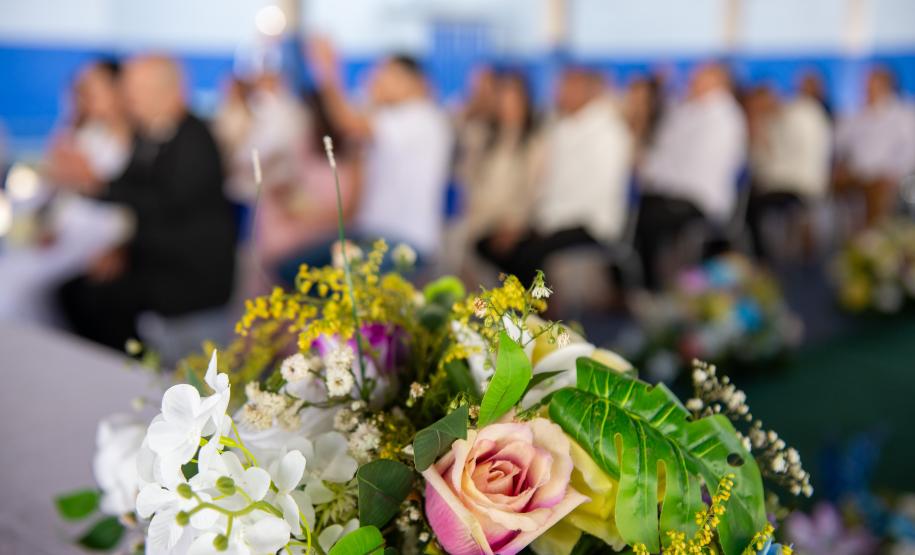 Imagem mostra arranjo de flores em primeiro plano e ao fundo os casais durante a cerimônia do Casando Direitos.