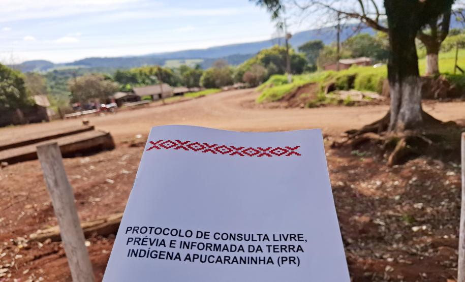 Imagem mostra o Protocolo de Consulta Livre, Prévia e Informada da Terra Indígena de Apucaraninha. Ao fundo se vê desfocada a comunidade.