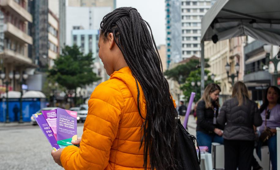 Mulher de costas segura os panfletos com informações sobre violência de gênero e onde procurar apoio.