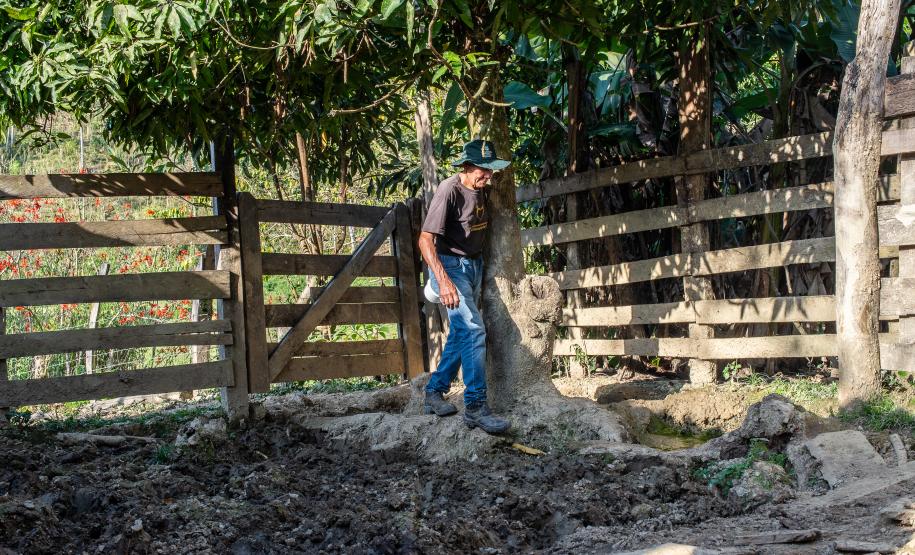 Agricultor passa por cerca de madeira para acessar área das criações.