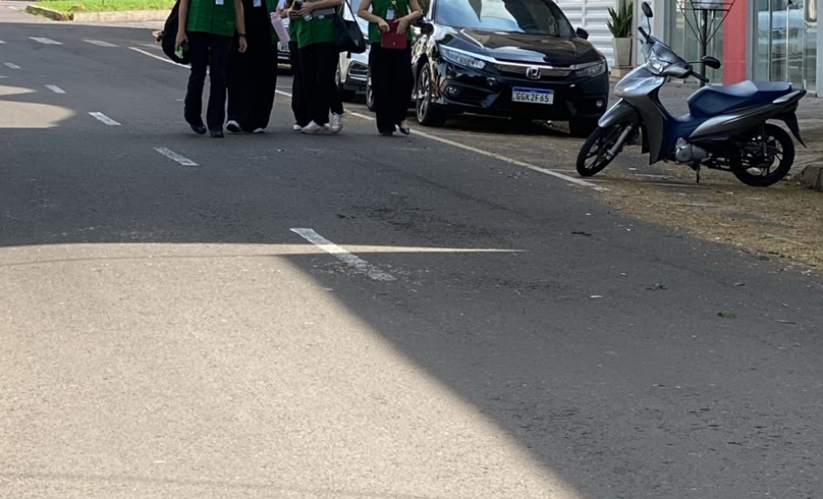 Quatro mulheres vestindo coletes verdes da Defensoria Pública caminham juntas e sorridentes por uma rua asfaltada. Elas seguram pastas e passam ao lado de veículos estacionados em uma área urbana.