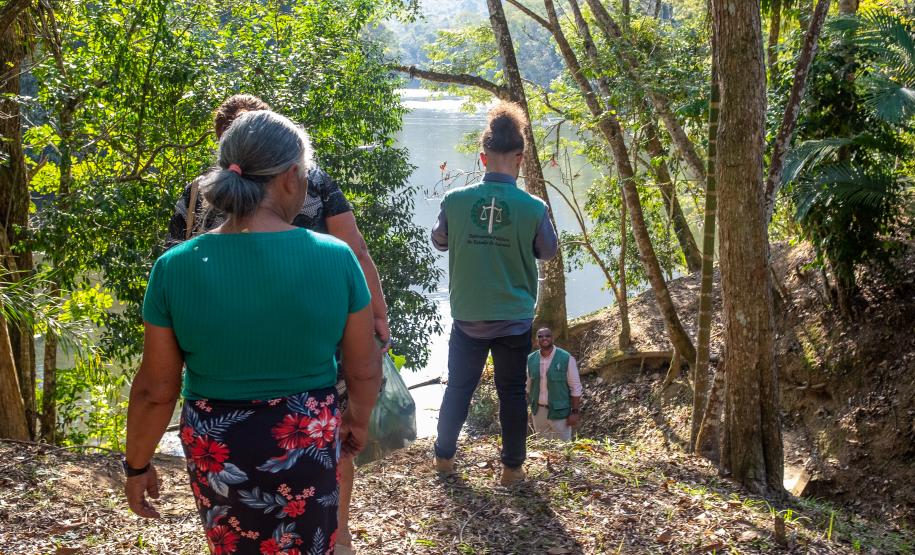 Imagem mostra mulher quilombola e um servidor da DPE-PR, ambos de costas, seguindo por trilha no quilombo.