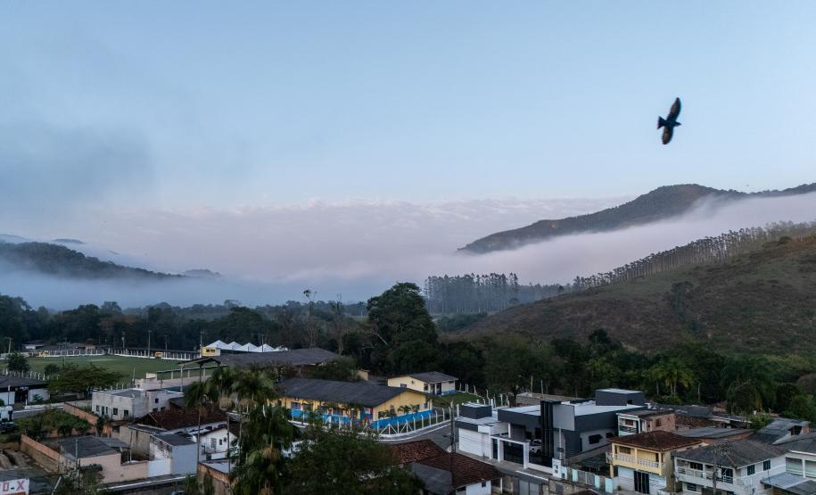 Imagem mostra vista aérea de Barra do Turvo, no Vale da Ribeira. No céu, um pássaro voa no canto esquerdo da imagem e a fundo montanhas cobertas por um mar de nuvens.
