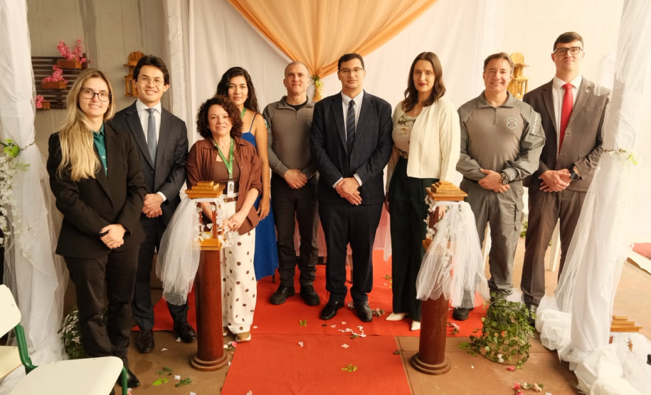 Nove pessoas posam para a foto. Quatro mulheres e cinco homens. Todos trajando roupas formais para os casamentos.