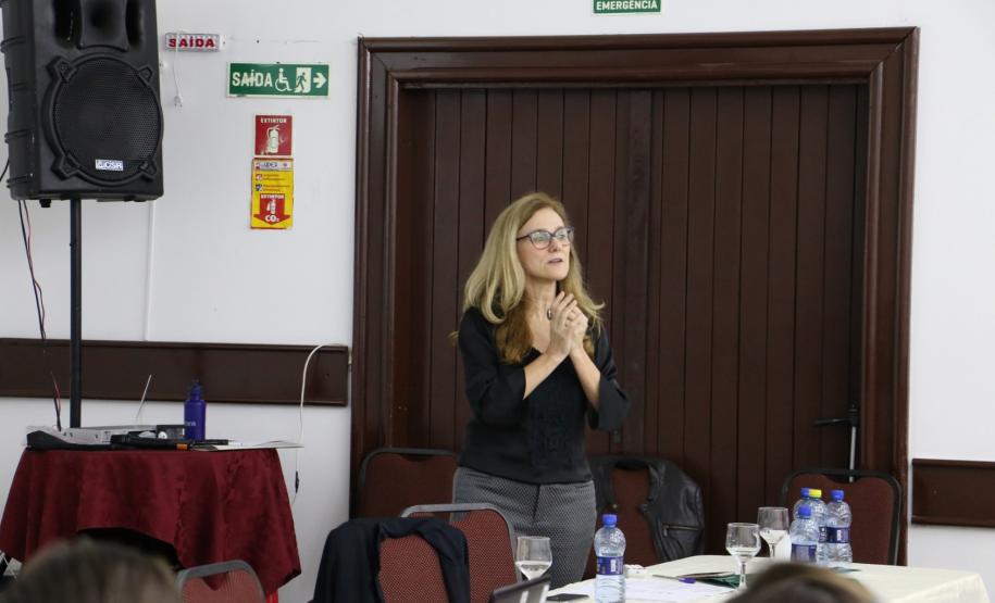 A Assistente Social do MPPR, Clarice Metzner, está de pé atrás da mesa principal para os palestrantes falando.