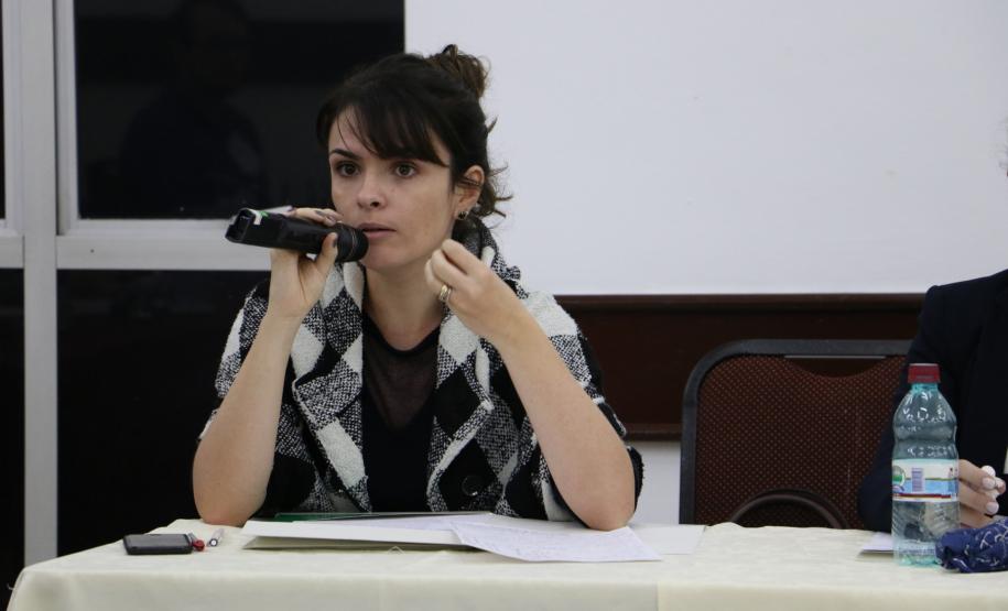 A imagem mostra a Dra. Flávia Palazzi, Diretora da EDEPAR, com um microfone próximo a sua boca sentada na ponta direita da mesa de palestrantes.