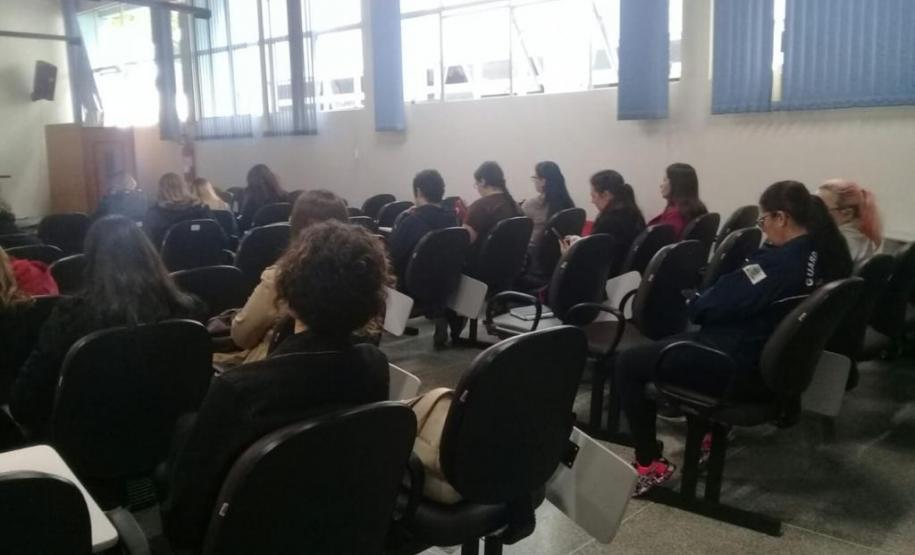 A imagem foi tirada no fundo da sala, focando nos ouvintes. Vemos esses de costas e sentados.