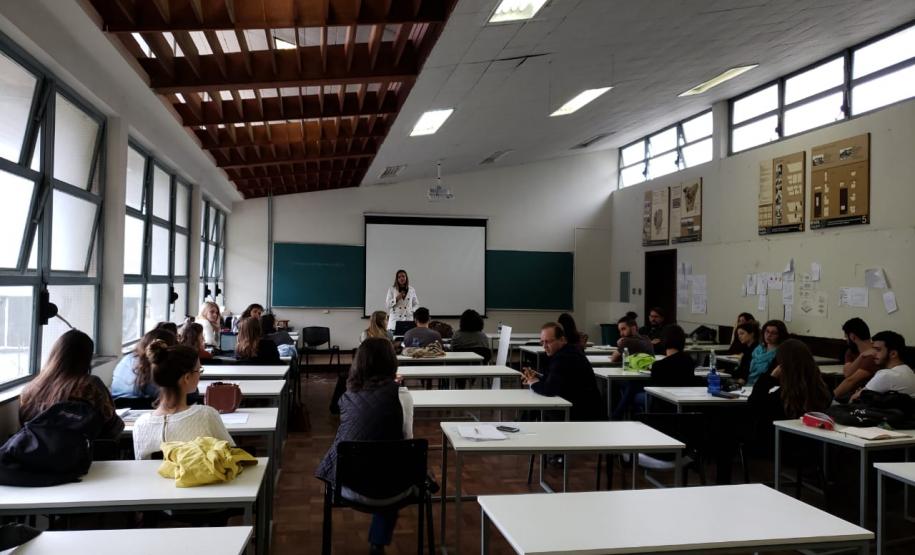 Em frente ao quadro, dra. Olenka Lins fala com os alunos que acompanham sua explicação.