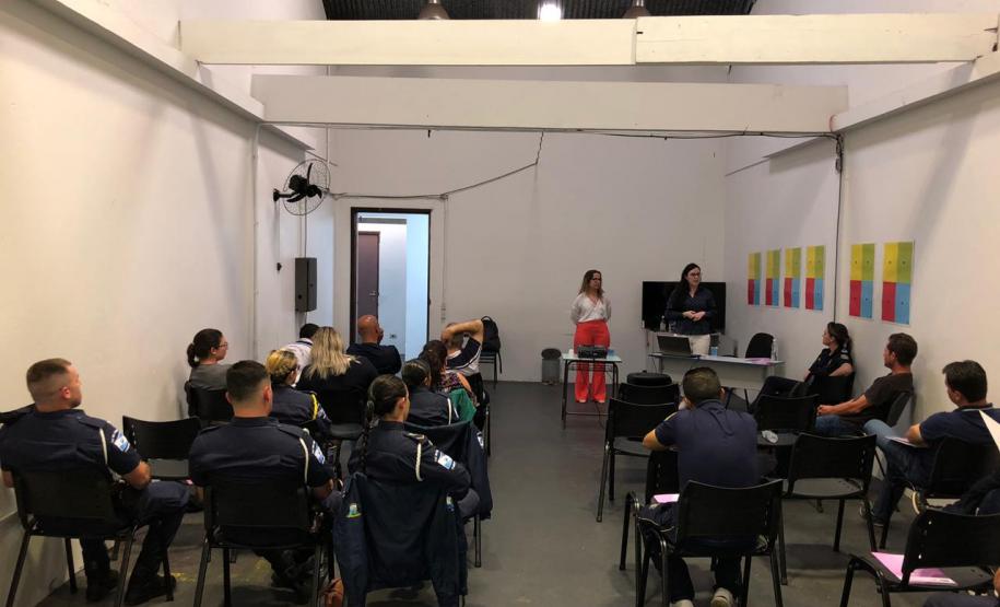 Na imagem vemos a equipe da DPPR palestrando aos guardas municipais. A equipe está de pé, ao fundo da sala, na frente dos oficias (esses estão sentados de costas).