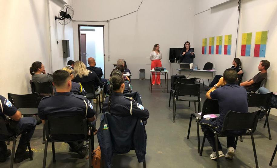 Na imagem vemos a equipe da DPPR palestrando aos guardas municipais. A equipe está de pé, ao fundo da sala, na frente dos oficias (esses estão sentados de costas).