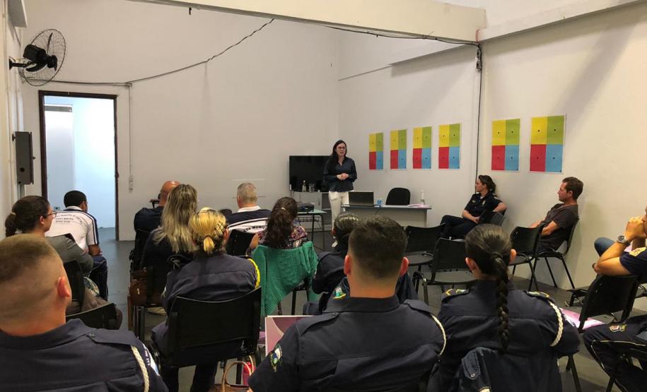 Na imagem vemos a equipe da DPPR palestrando aos guardas municipais. A equipe está de pé, ao fundo da sala, na frente dos oficias (esses estão sentados de costas).
